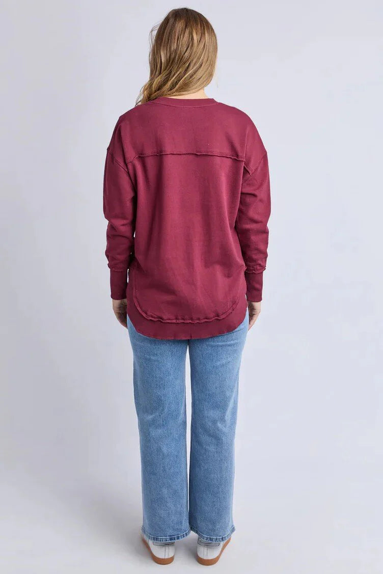 Woman wearing a Foxwood Simplified Metallic crew in burgundy paired with denim jeans on a plain background