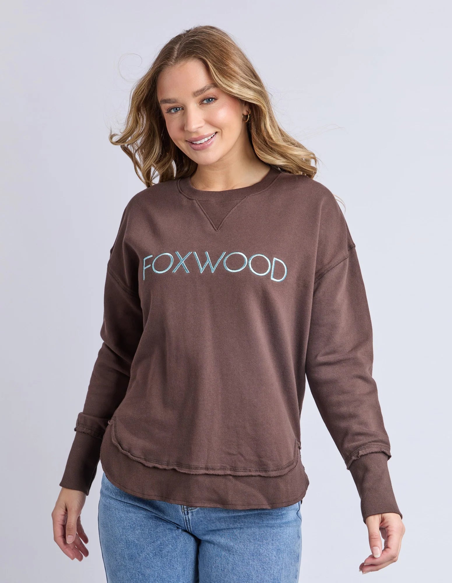 Image of Woman wearing a brown sweatshirt with 'FOXWOOD' logo on a plain background