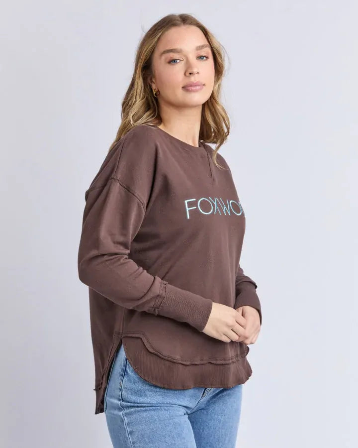 Woman wearing a brown sweatshirt with 'FORWARD' text on a plain background