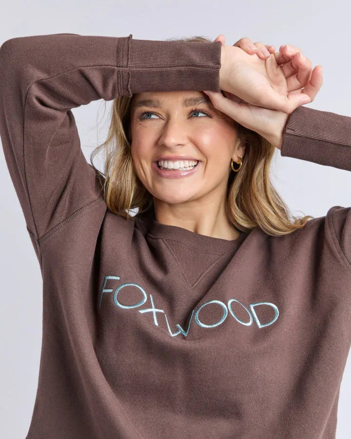Woman wearing a brown sweatshirt with 'FOXWOOD' printed on it against a light gray background