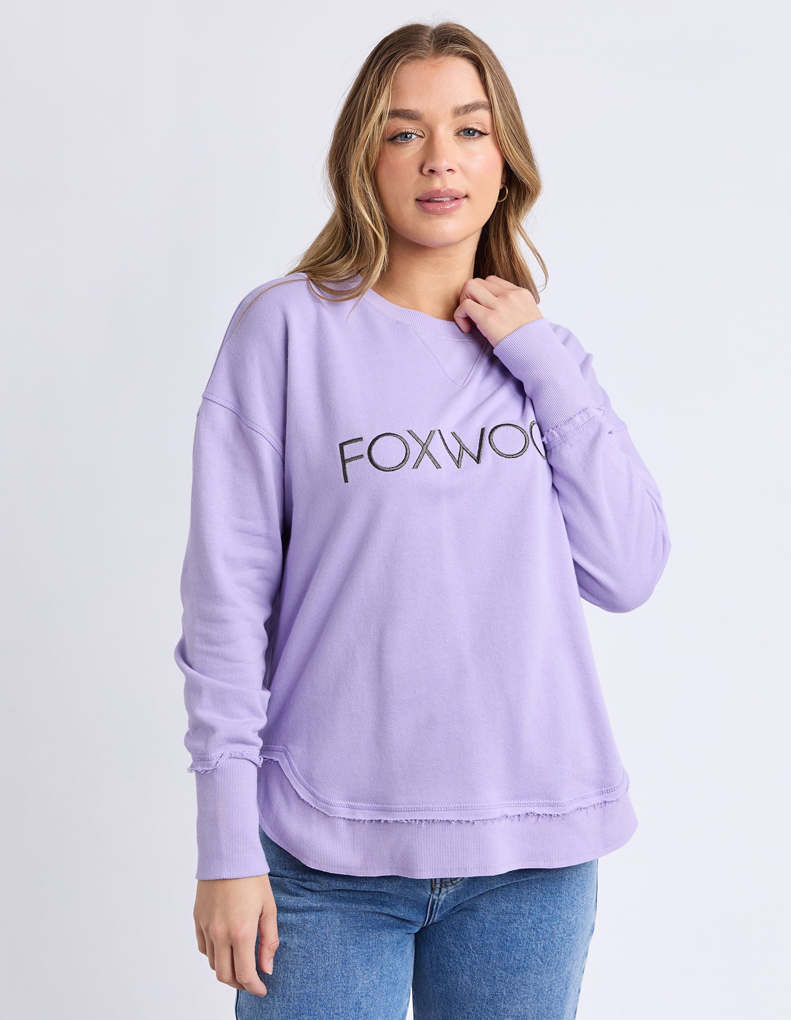 Woman wearing a lavender jumper with 'FOXWOOD' logo on a light grey background