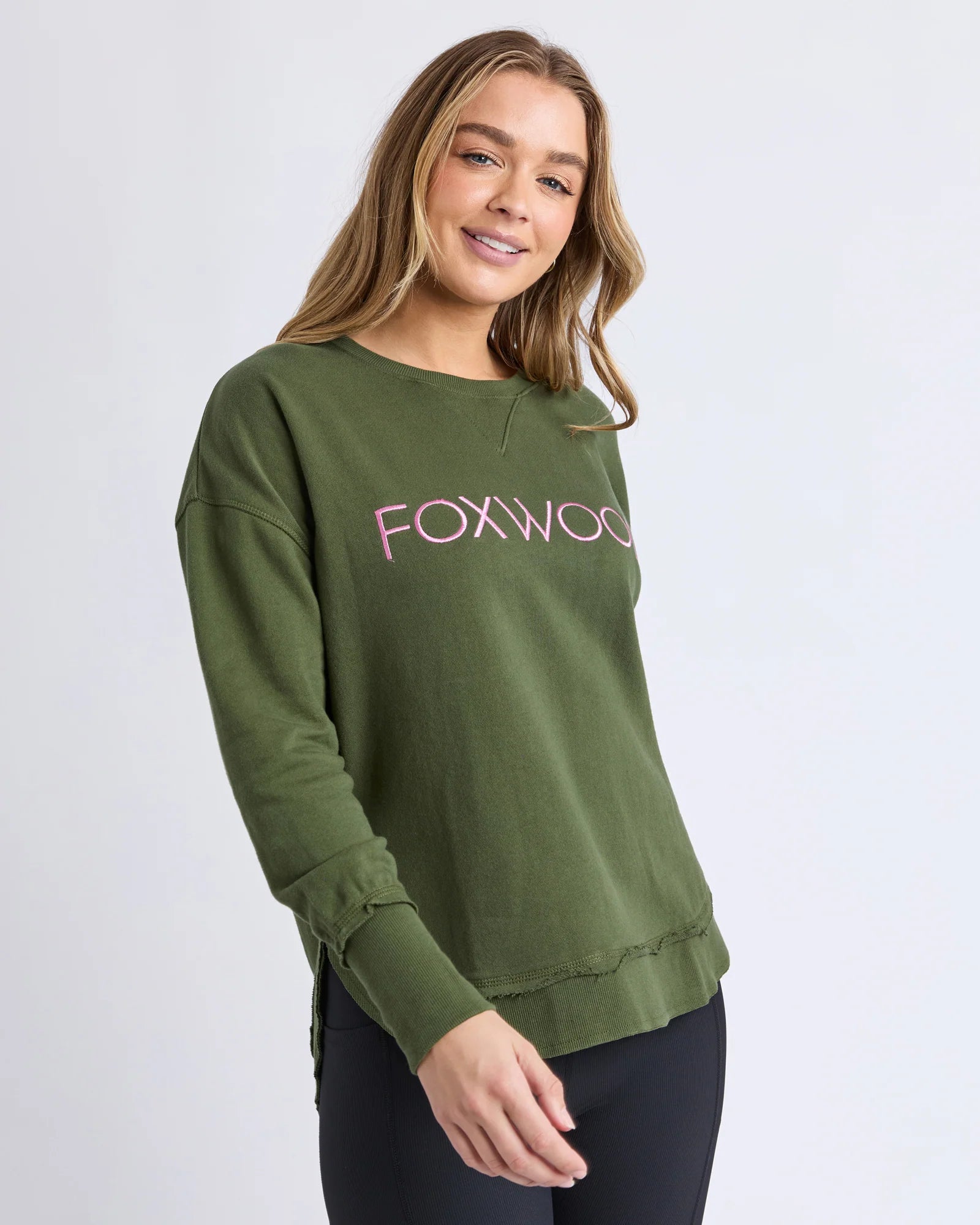 Image of Woman wearing a Foxwood green sweatshirt with 'FOXWOOD' printed in pink on a white background