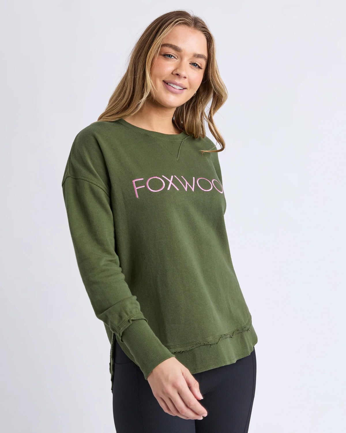 Woman wearing a Foxwood green sweatshirt with 'FOXWOOD' printed in pink on a white background