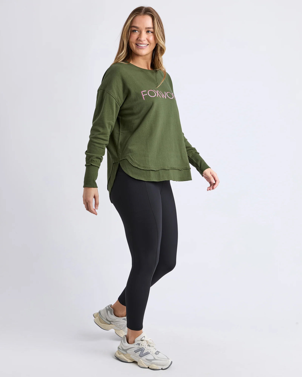 Woman wearing a Foxwood green sweatshirt and black leggings on a white background