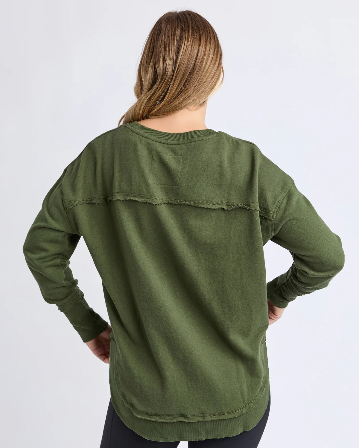 A woman viewed from the back wearing a Foxwood olive green long-sleeve top with a relaxed fit and a horizontal seam detail across the upper back, set against a plain light gray studio background.