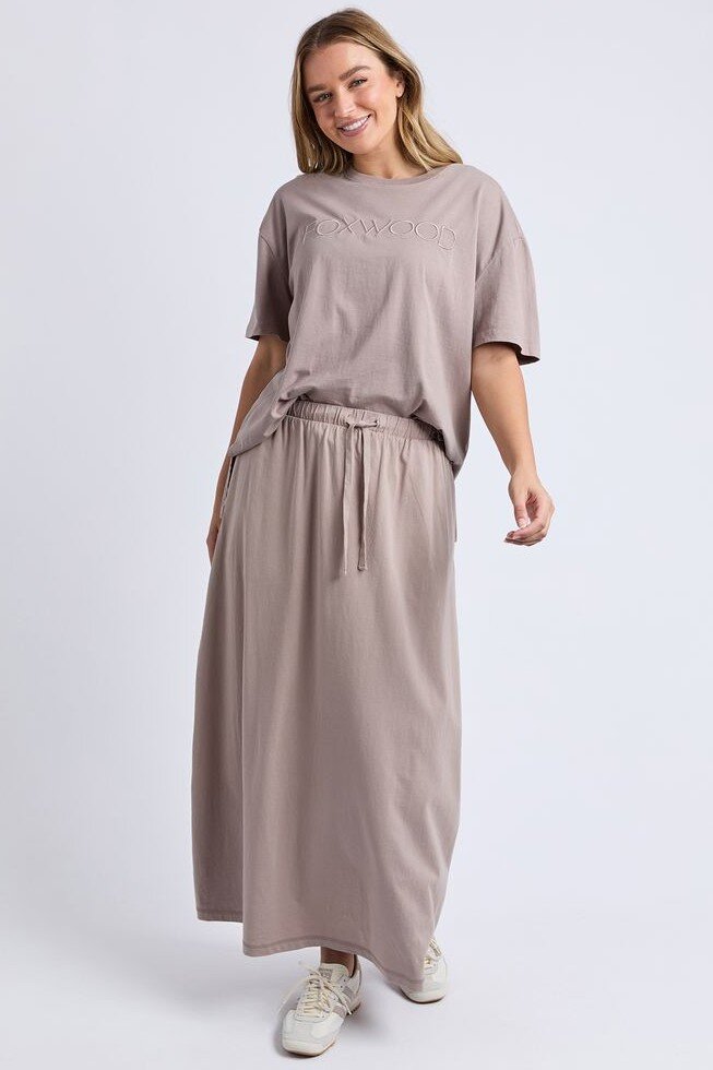 Image of A woman modeling a matching Foxwood taupe two-piece lounge set consisting of a short-sleeve t-shirt with tonal embroidery and matching wide-leg drawstring trousers, paired with white sneakers against a light gray studio background.
