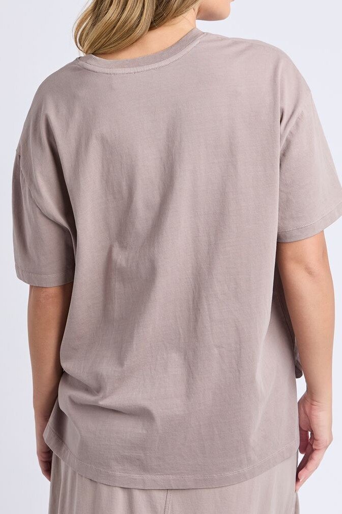 A woman shown from the back wearing an Foxwood oversized short-sleeve crew-neck t-shirt in a muted taupe-gray color, paired with matching bottoms against a plain light gray studio background.