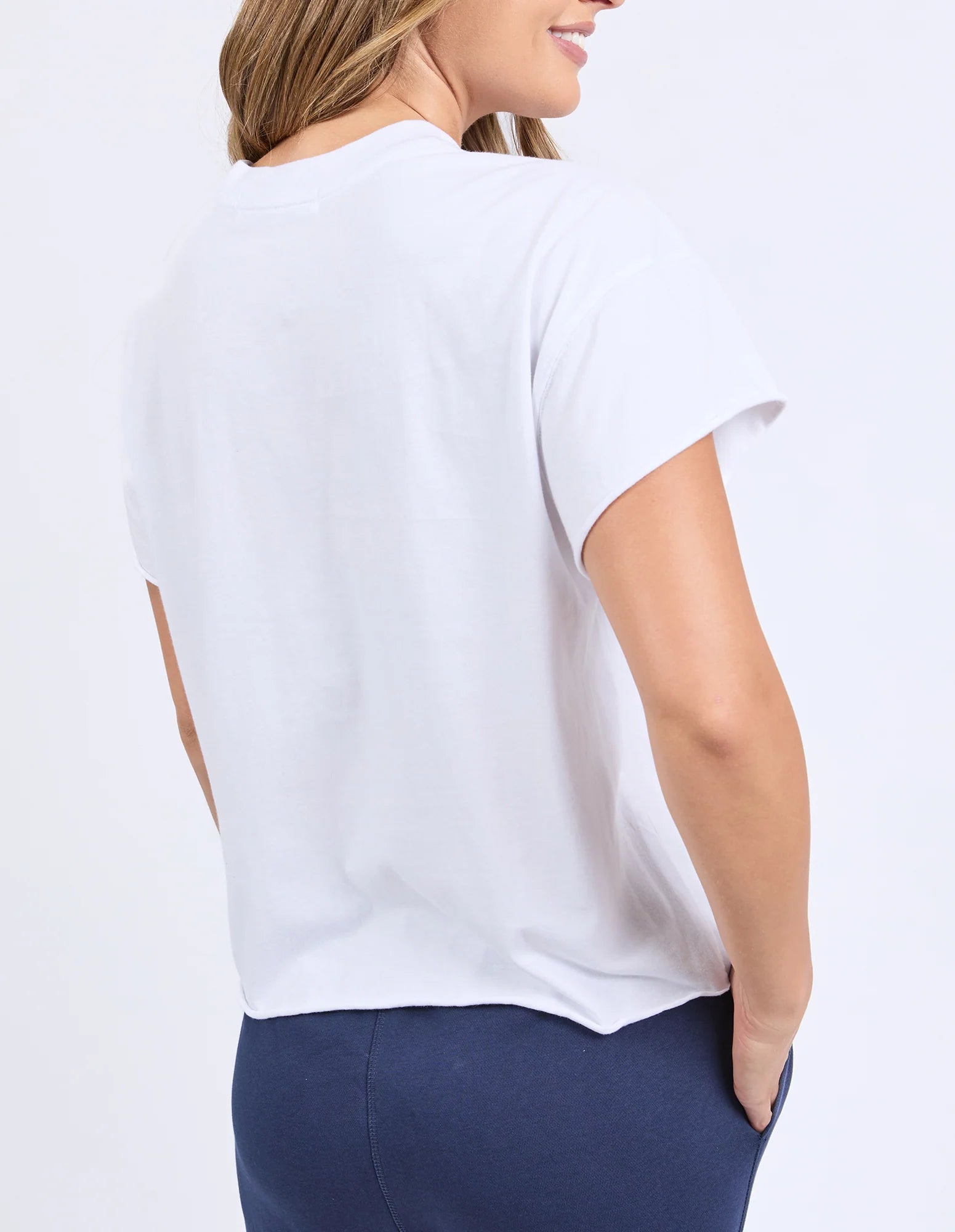 Image of A woman shown from the back wearing a Foxwood plain white short-sleeve crewneck T-shirt and navy blue pants against a clean white studio background.