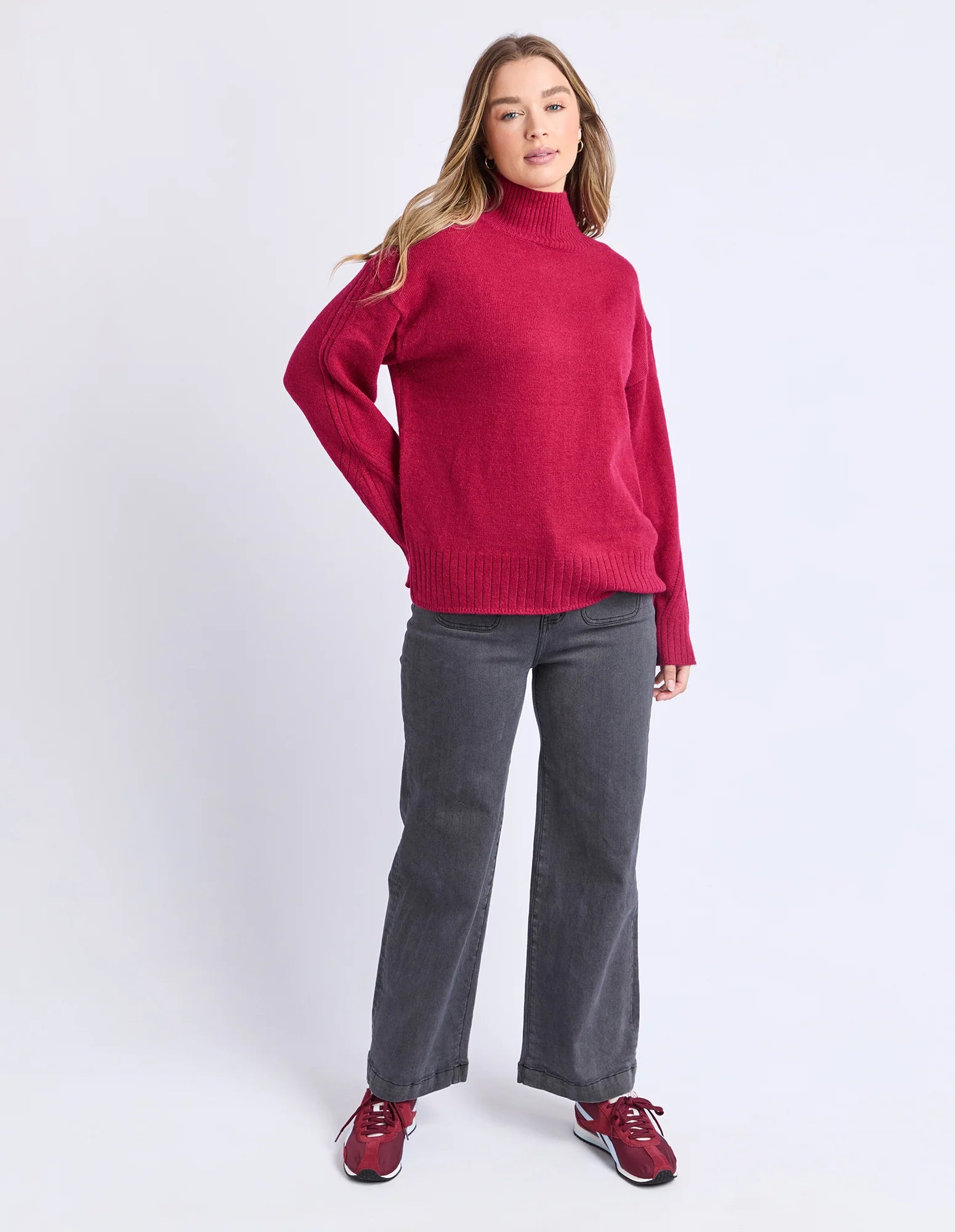 Woman wearing a Foxwood red sweater and gray pants on a white background