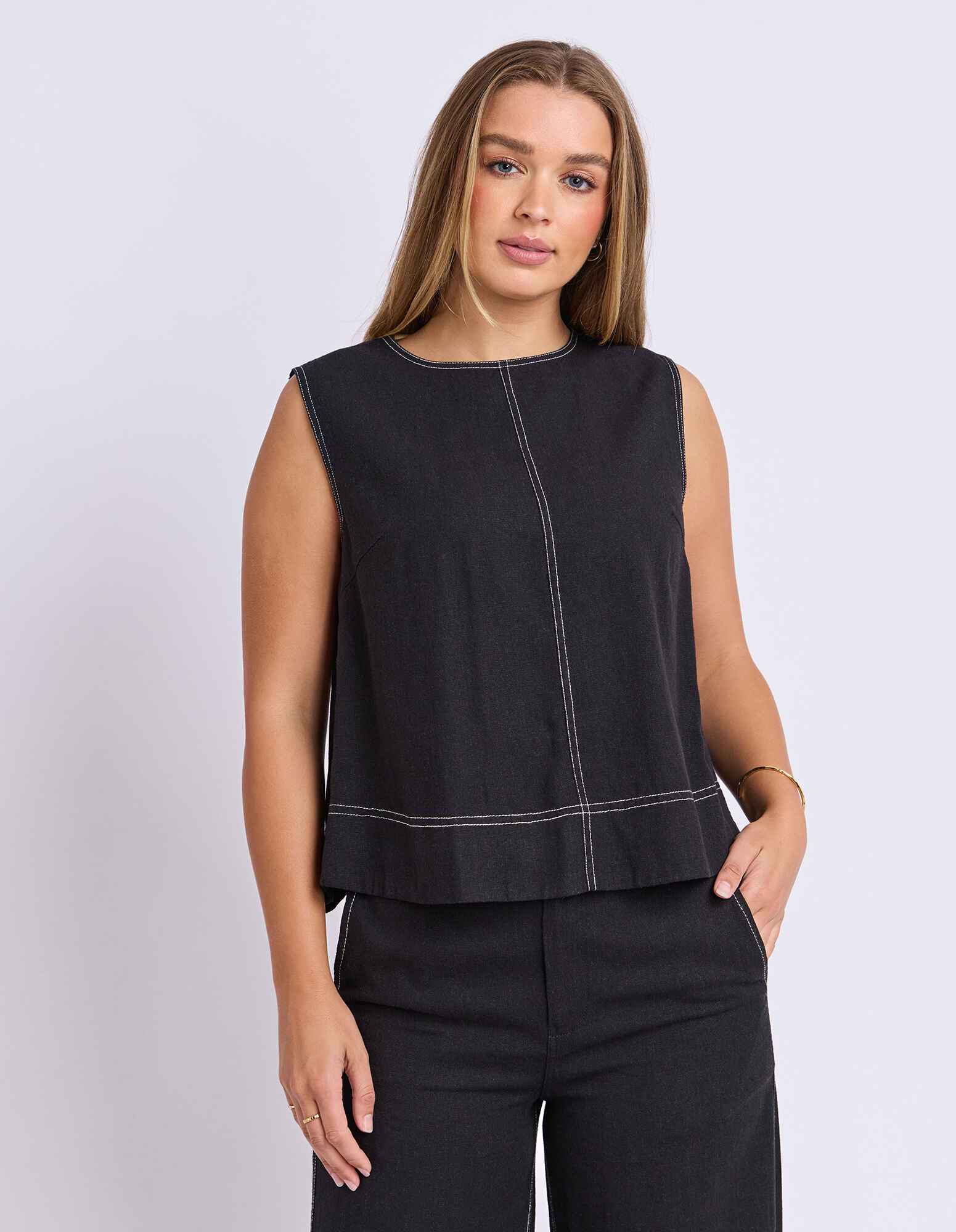 Image of Woman wearing a Foxwood black sleeveless top with white stitching on a light gray background