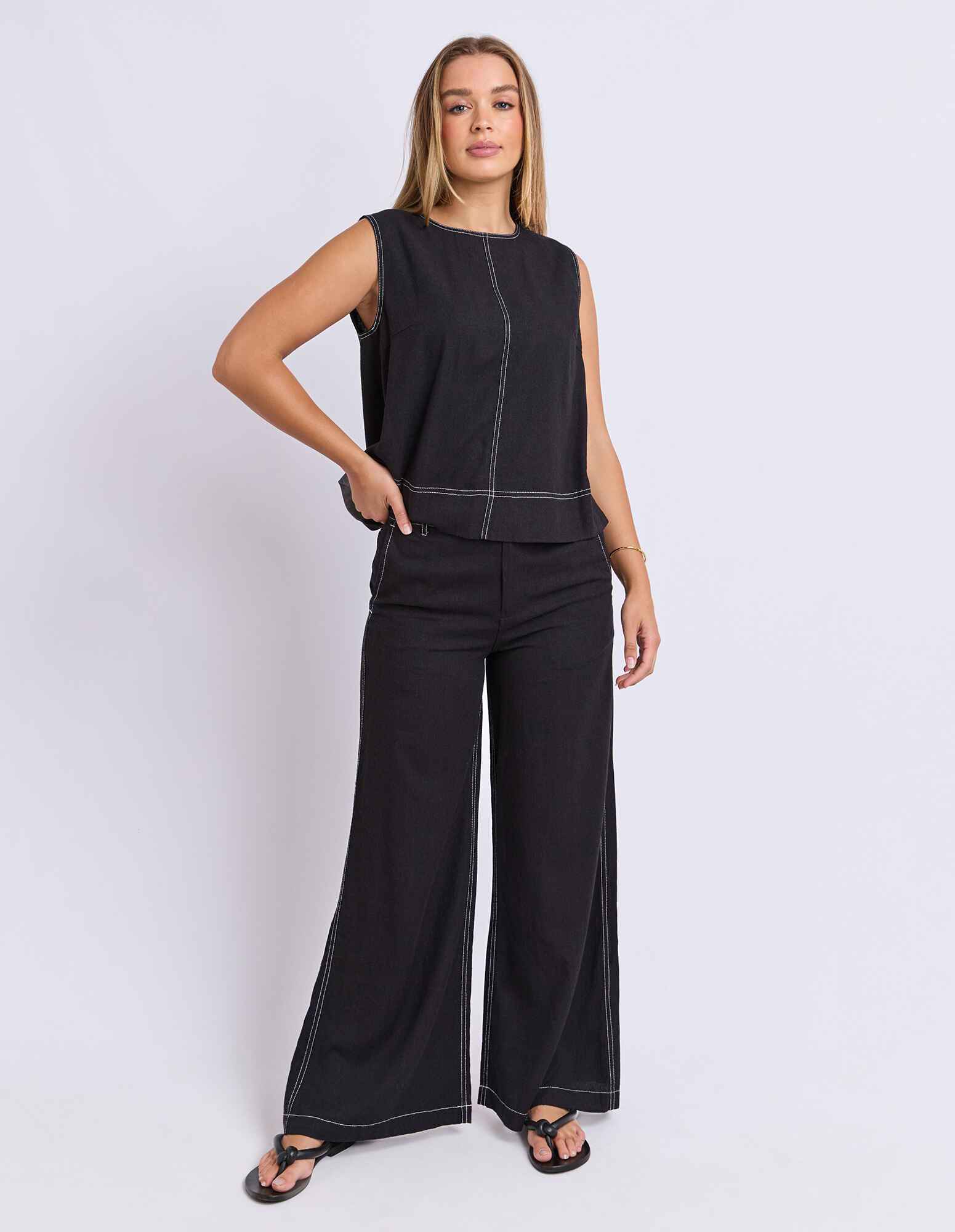 Image of Woman wearing a Foxwood black sleeveless top and wide-leg pants on a white background