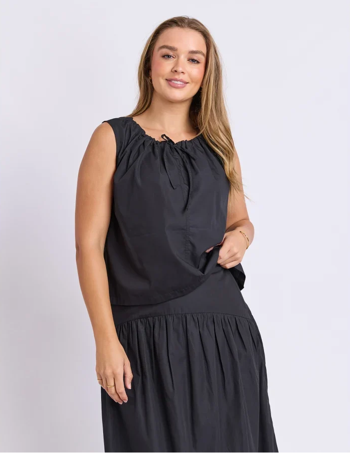 Image of Woman wearing a Foxwood set. Pictured is a singlet with tie detailing paired with the matching black skirt on a plain background