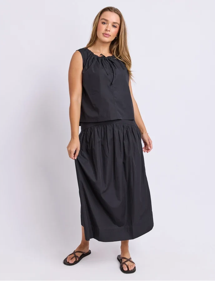 Image of Woman wearing a Foxwood set. Pictured is a singlet with tie detailing paired with the matching black skirt on a plain background