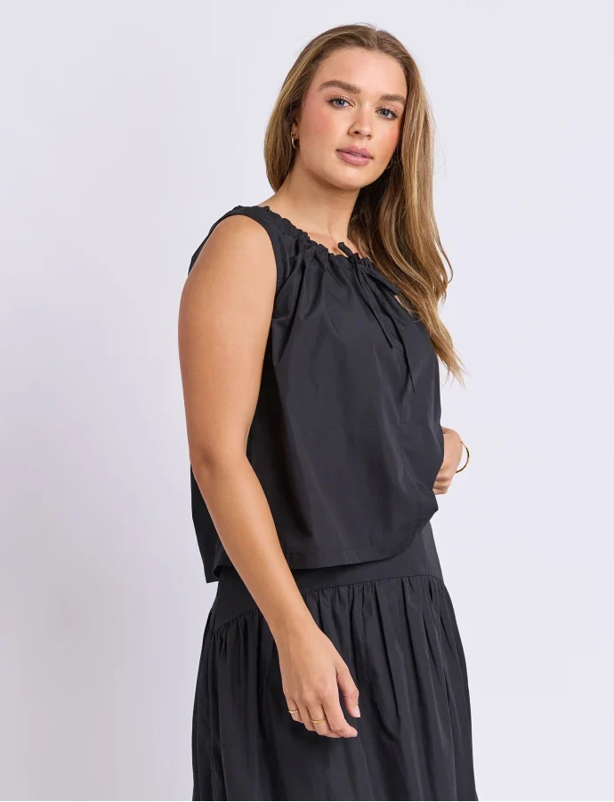 Image of Woman wearing a Foxwood set. Pictured is a singlet with tie detailing paired with the matching black skirt on a plain background