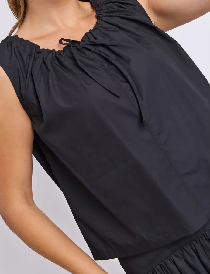 Image of Woman wearing a Foxwood set. Pictured is a singlet with tie detailing paired with the matching black skirt on a plain background
