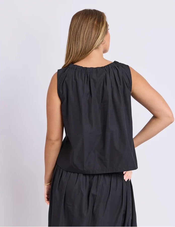 Woman wearing a Foxwood set. Pictured is a singlet with tie detailing paired with the matching black skirt on a plain background