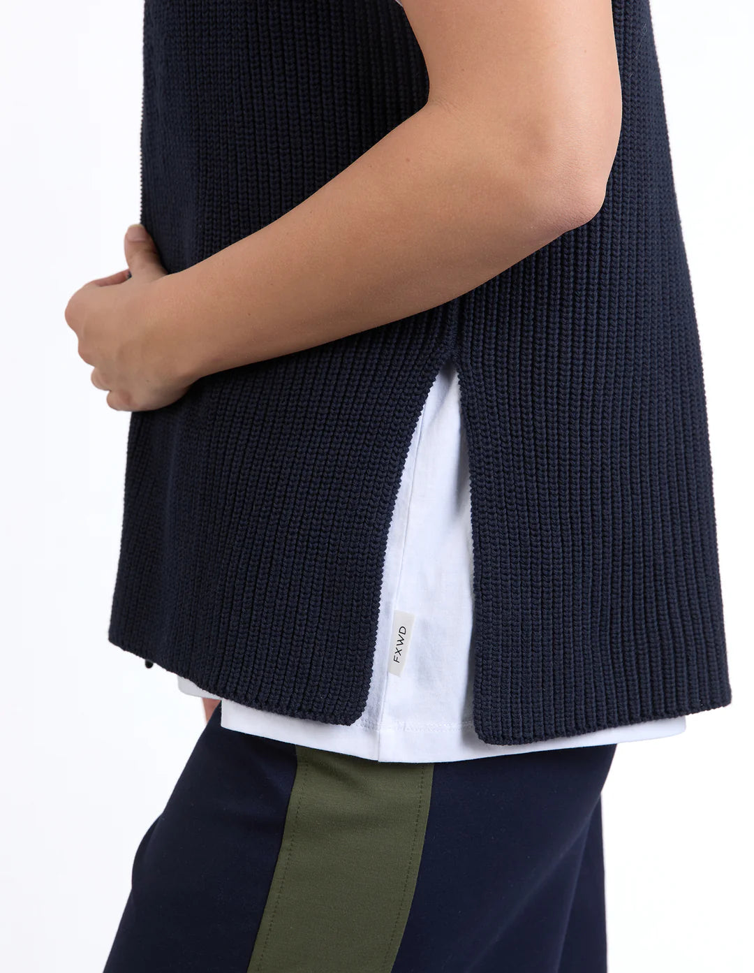 Image of Woman wearing a Foxwood dark blue knitted vest over a white shirt with green pants on a white background
