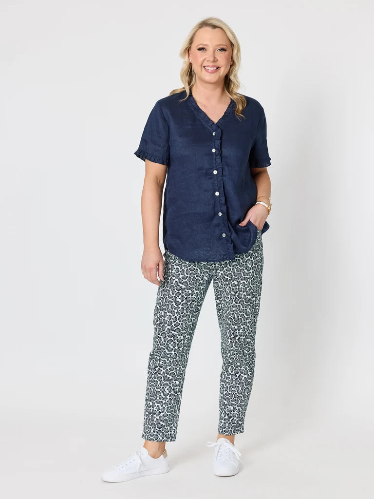 Image of A woman modeling a Gordon Smith navy blue short-sleeve button-up shirt and patterned pants with white sneakers, standing against a light gray studio background.