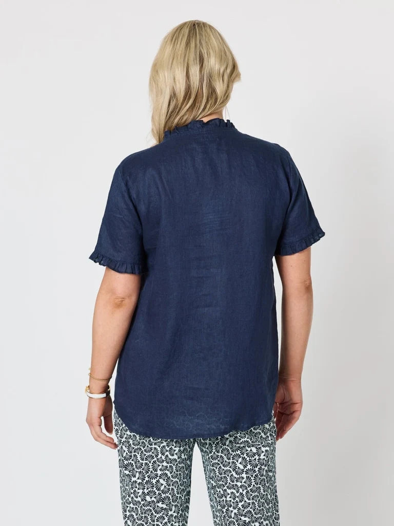 Image of A woman viewed from the back wearing a Gordon Smith dark navy blue short-sleeve linen shirt with ruffled cuffs and patterned gray and white pants, against a light gray studio background.