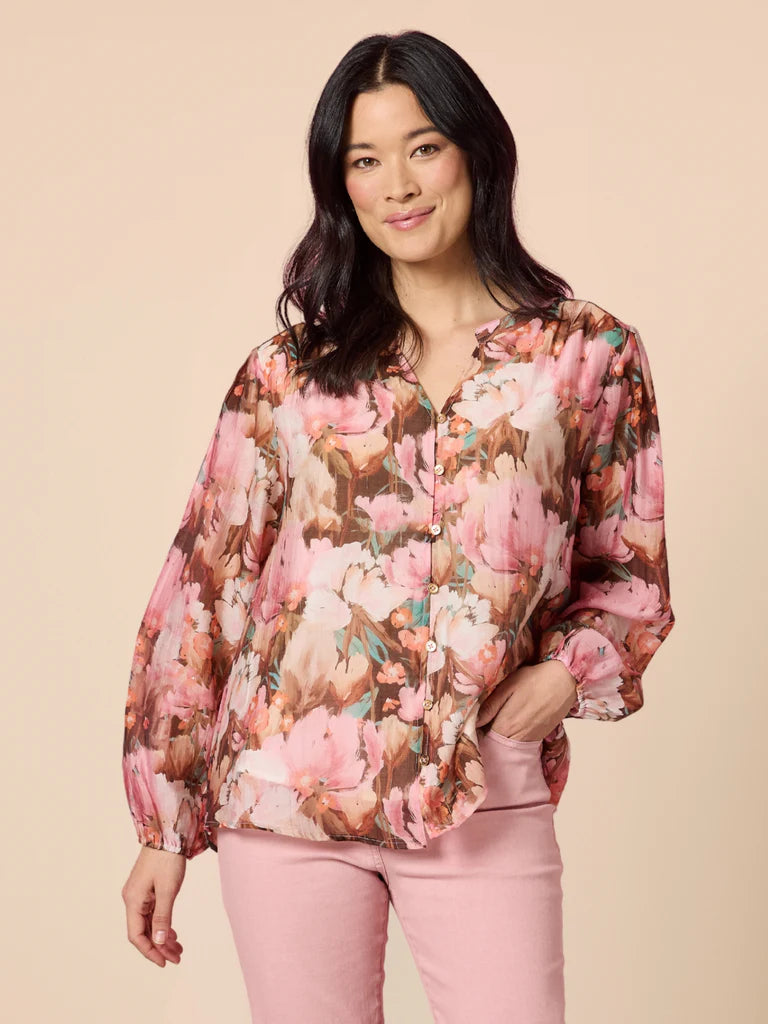 Woman wearing a Gordon Smith floral blouse and pink pants against a beige background
