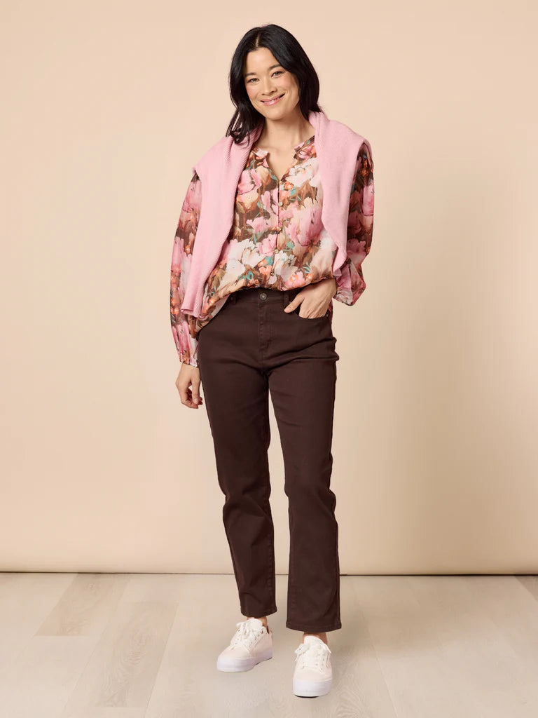 Image of Woman wearing a Gordon Smith floral blouse, pink vest, brown pants, and white sneakers on a beige background