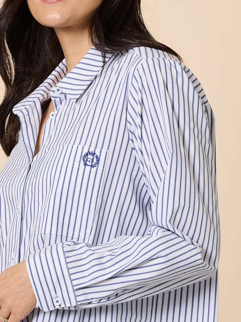 Close-up of a woman wearing a Gordon Smith blue and white striped shirt with a logo on a beige background