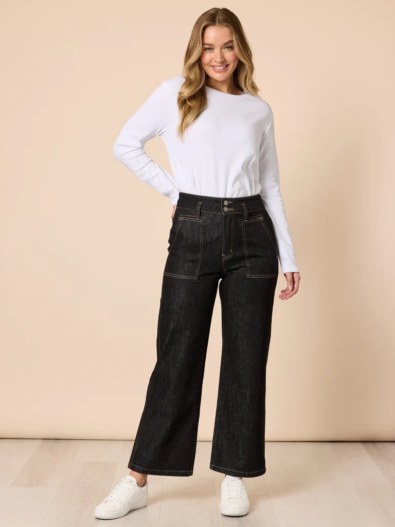Woman wearing Gordon Smith black wide-leg jeans and a white long-sleeve top against a beige background