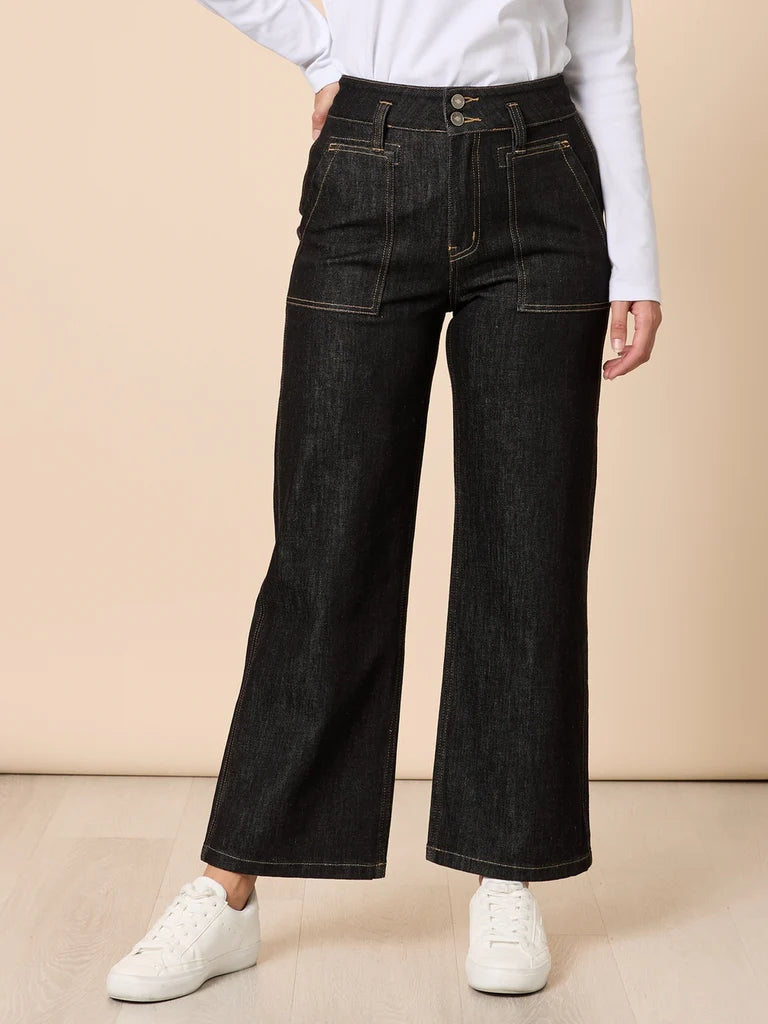 Woman wearing Gordon Smith black wide-leg jeans and white sneakers on a beige background