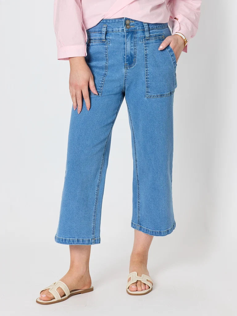 Image of A woman wearing Gordon Smith light blue cropped denim jeans with a pink shirt and beige slide sandals, standing against a plain light gray studio background.