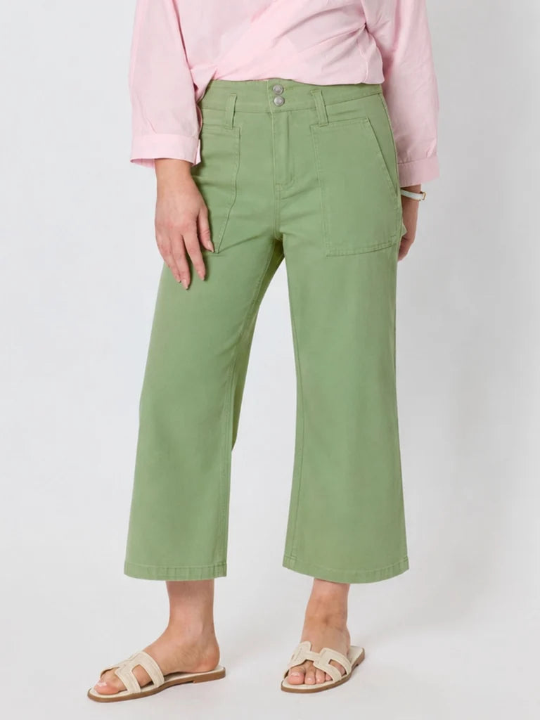 Image of A woman wearing Gordon Smith sage green cropped pants with a pink shirt and beige slide sandals, standing against a light gray studio background.