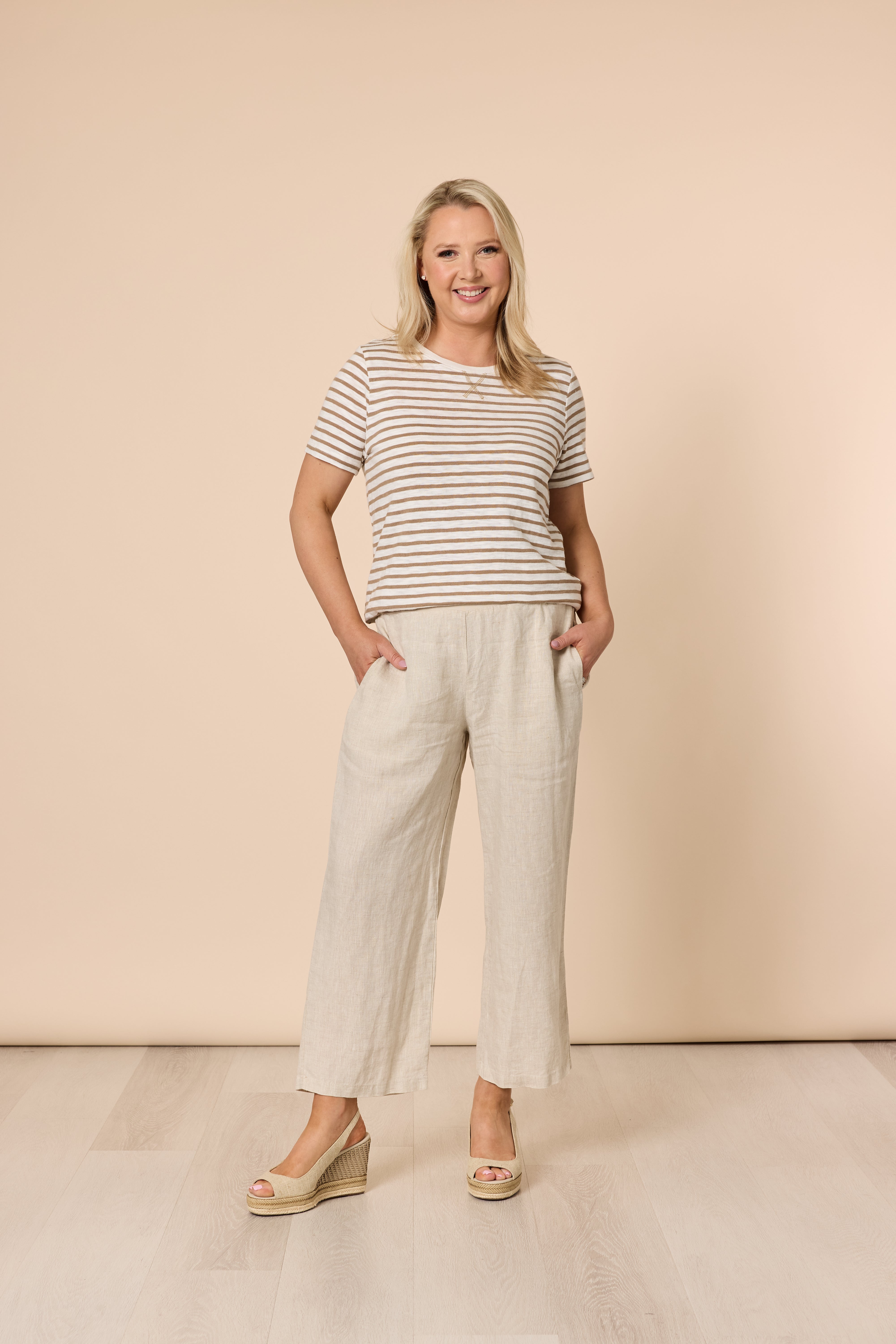 Image of Woman wearing a striped shirt and Gordon Smith beige pants against a beige background