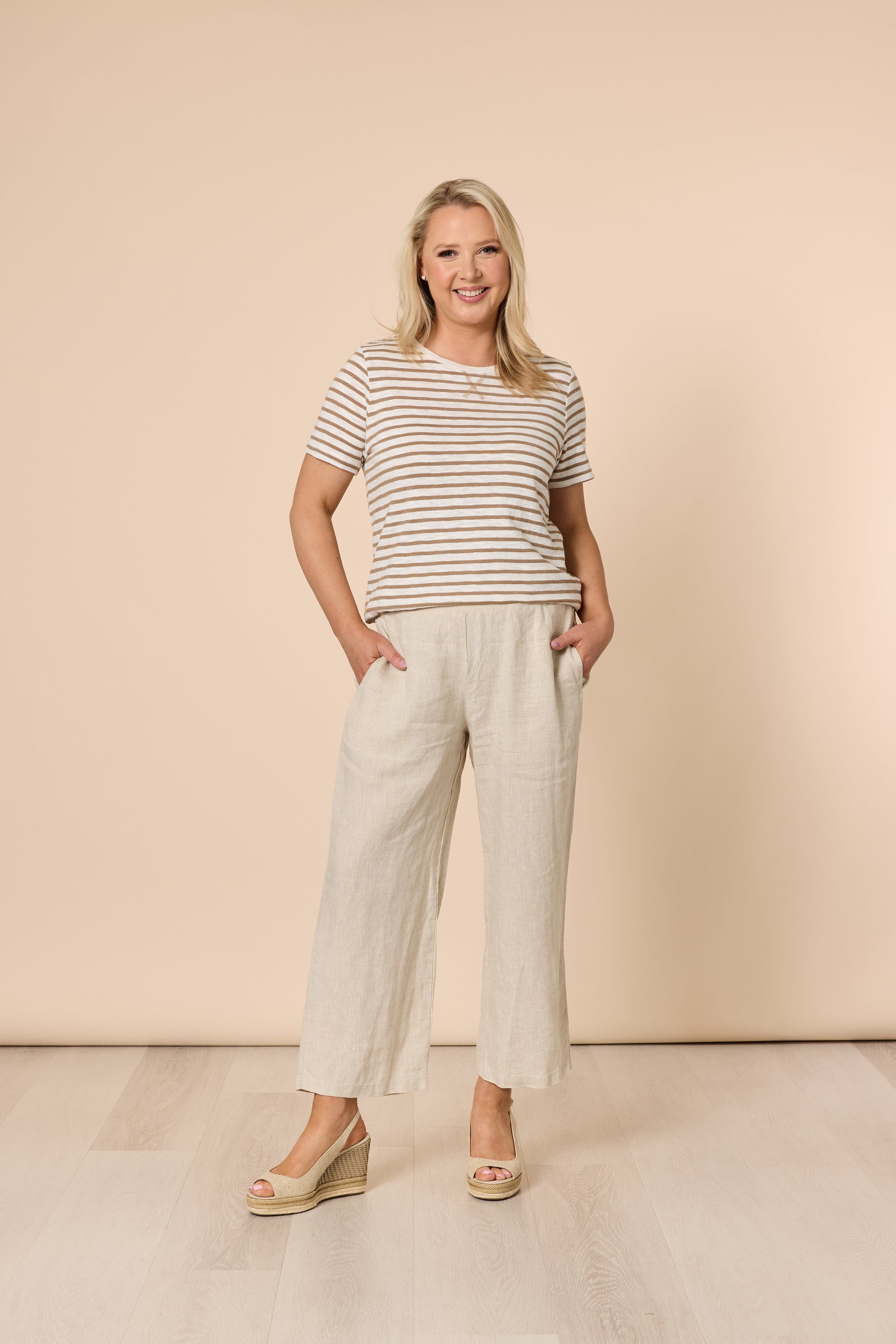 Woman wearing a striped shirt and Gordon Smith beige pants against a beige background