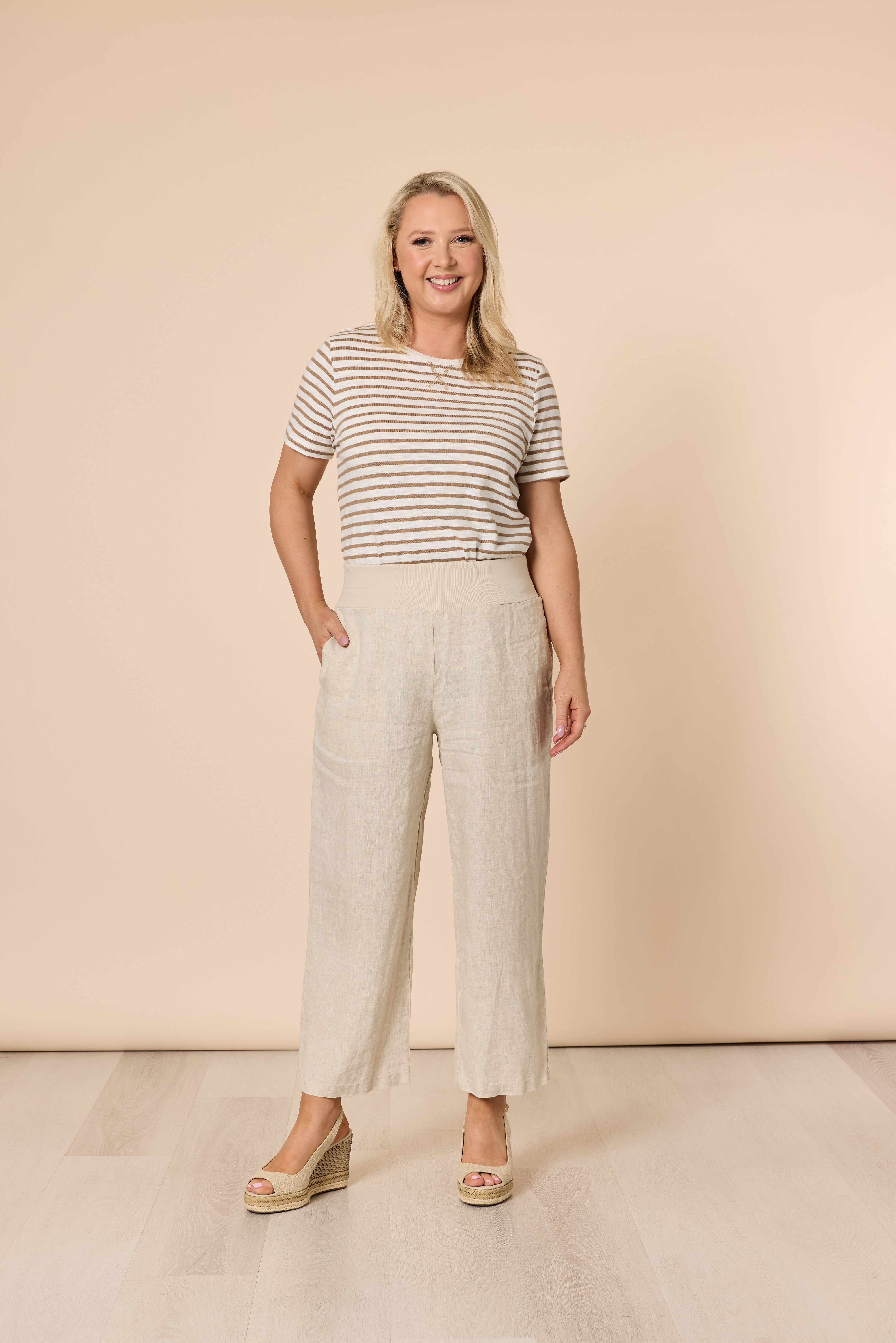 Image of Woman wearing a striped shirt and Gordon Smith light-colored pants against a beige background