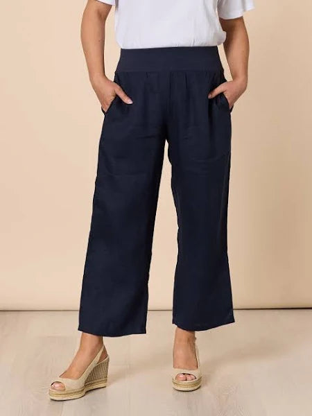 Woman wearing Gordon Smith navy wide-leg pants and a white top on a beige background