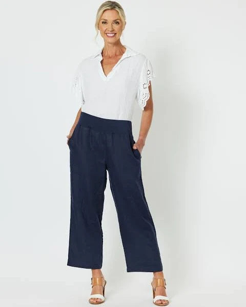 Woman wearing a white top with lace sleeves and Gordon Smith navy pants on a white background