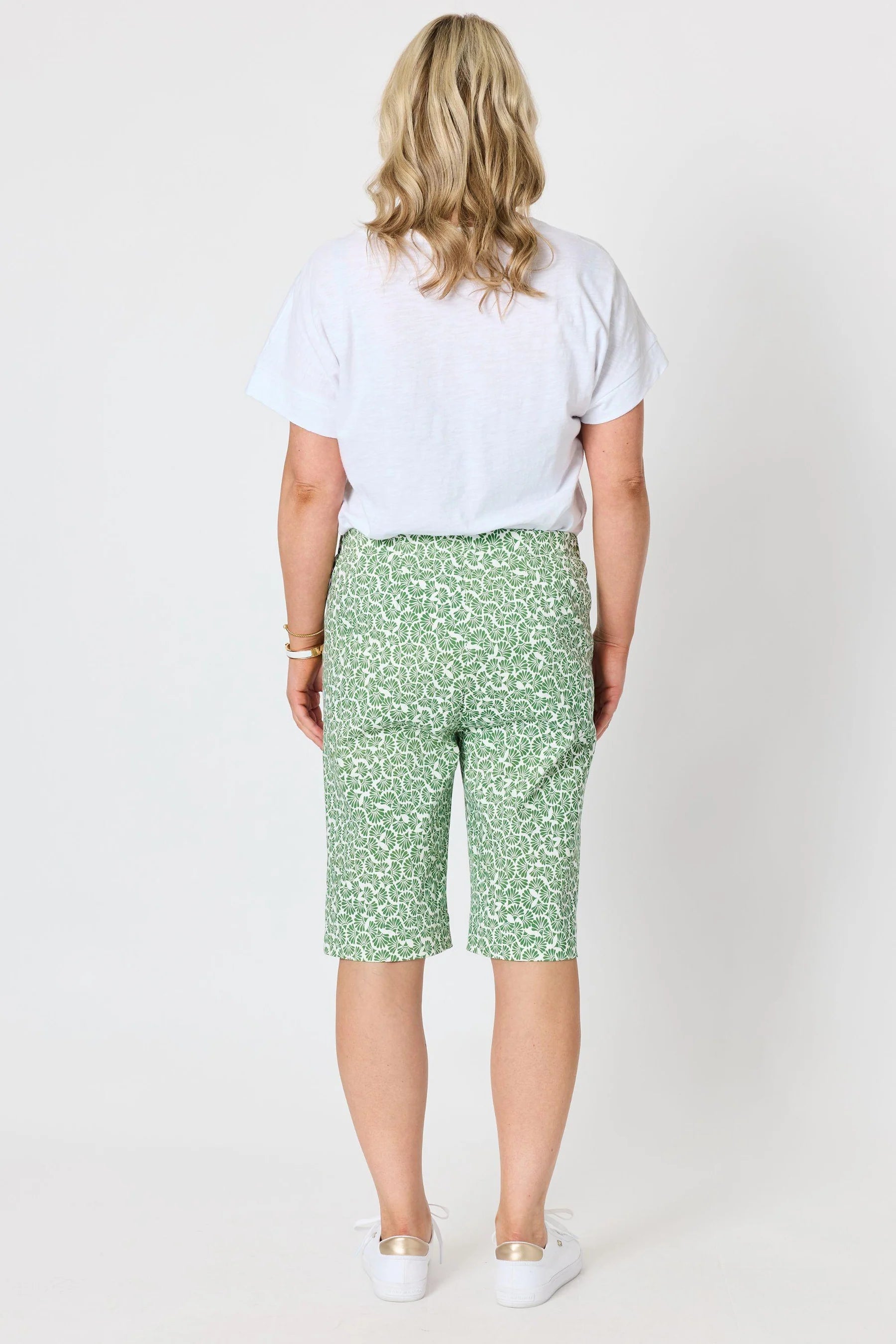 Image of A woman shown from the back wearing a Gordon Smith white t-shirt and green shorts with a white abstract pattern, standing against a light gray studio background.