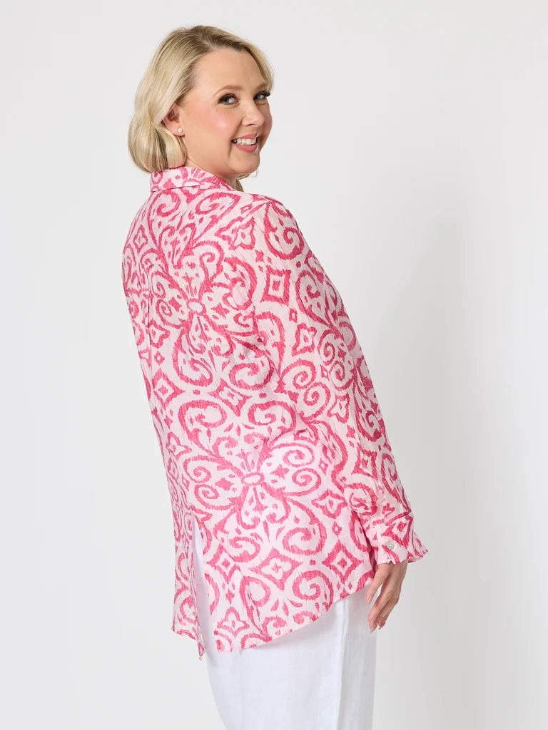 Image of A woman with blonde hair is shown from a side-back angle wearing a Gordon Smith pink and white patterned long-sleeve shirt and white pants against a plain white studio background.