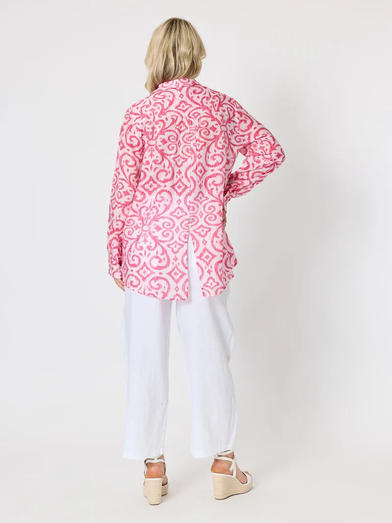 Image of A woman shown from the back wearing a Gordon Smith pink and white patterned long-sleeve shirt, white pants, and beige wedge sandals against a plain light gray studio background.