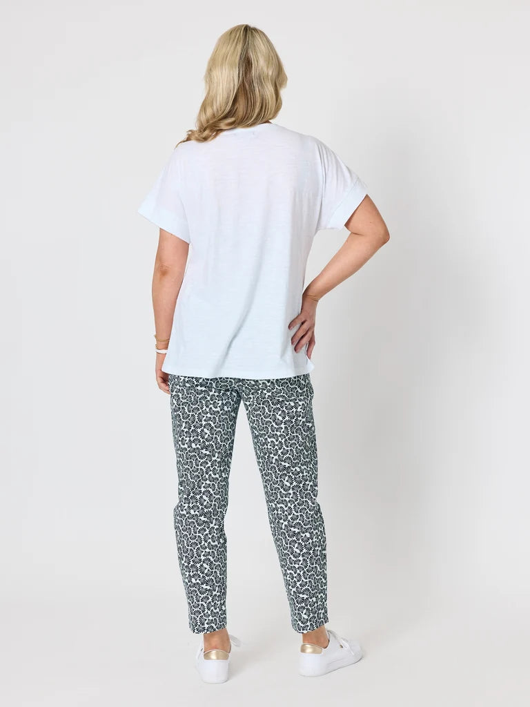 A woman shown from the back wearing a Gordon Smith white t-shirt and black-and-white patterned pants, standing against a light gray studio background.