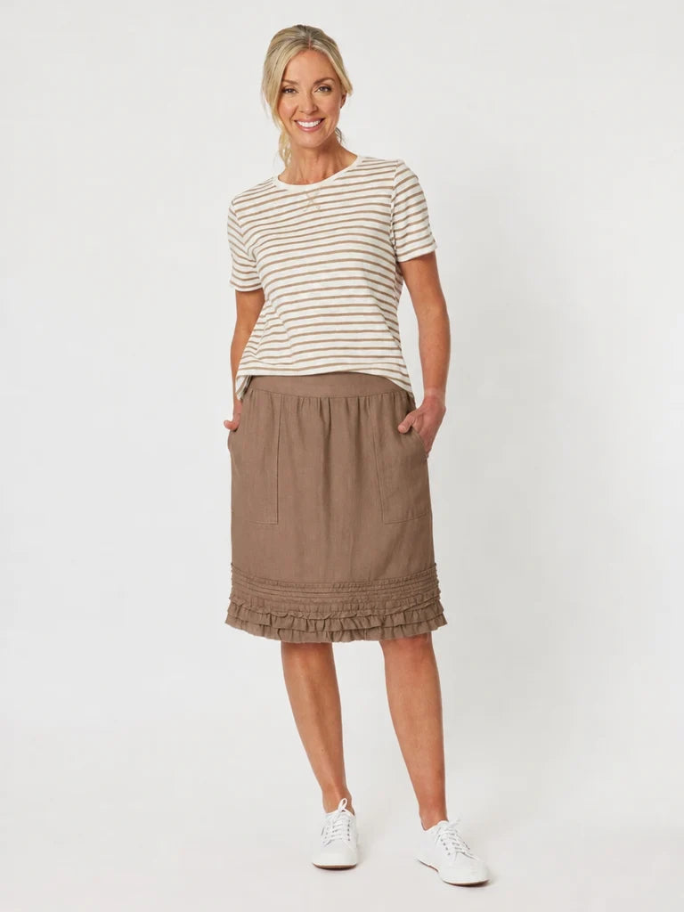 Image of A woman modeling a short-sleeve beige and white striped t-shirt with a Gordon Smith brown midi skirt featuring a ruffled hem, paired with white sneakers, against a plain light gray background.