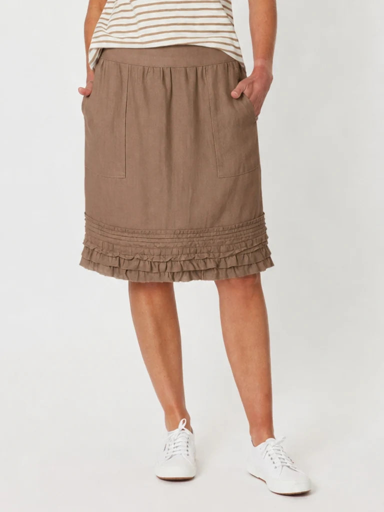 Image of A woman wearing a Gordon Smith brown ruffled knee-length skirt with side pockets, paired with a cream and brown striped top and white sneakers, shown from the waist down against a light gray studio background.
