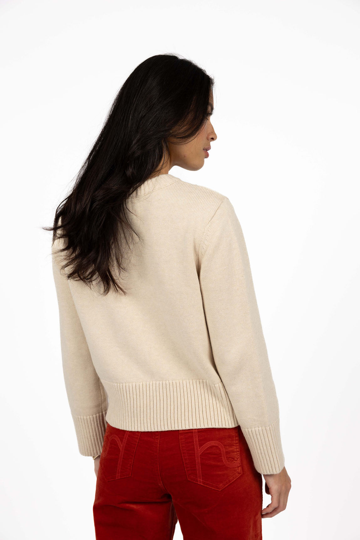 Woman wearing a Humidity beige sweater and red pants on a white background