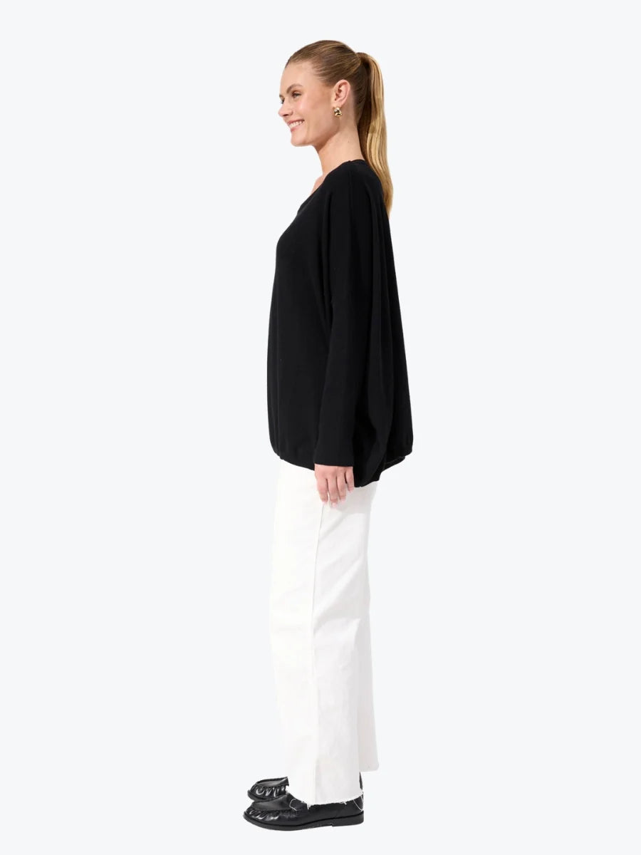 Woman wearing black Haven knit paired with white jeans on a plain background 