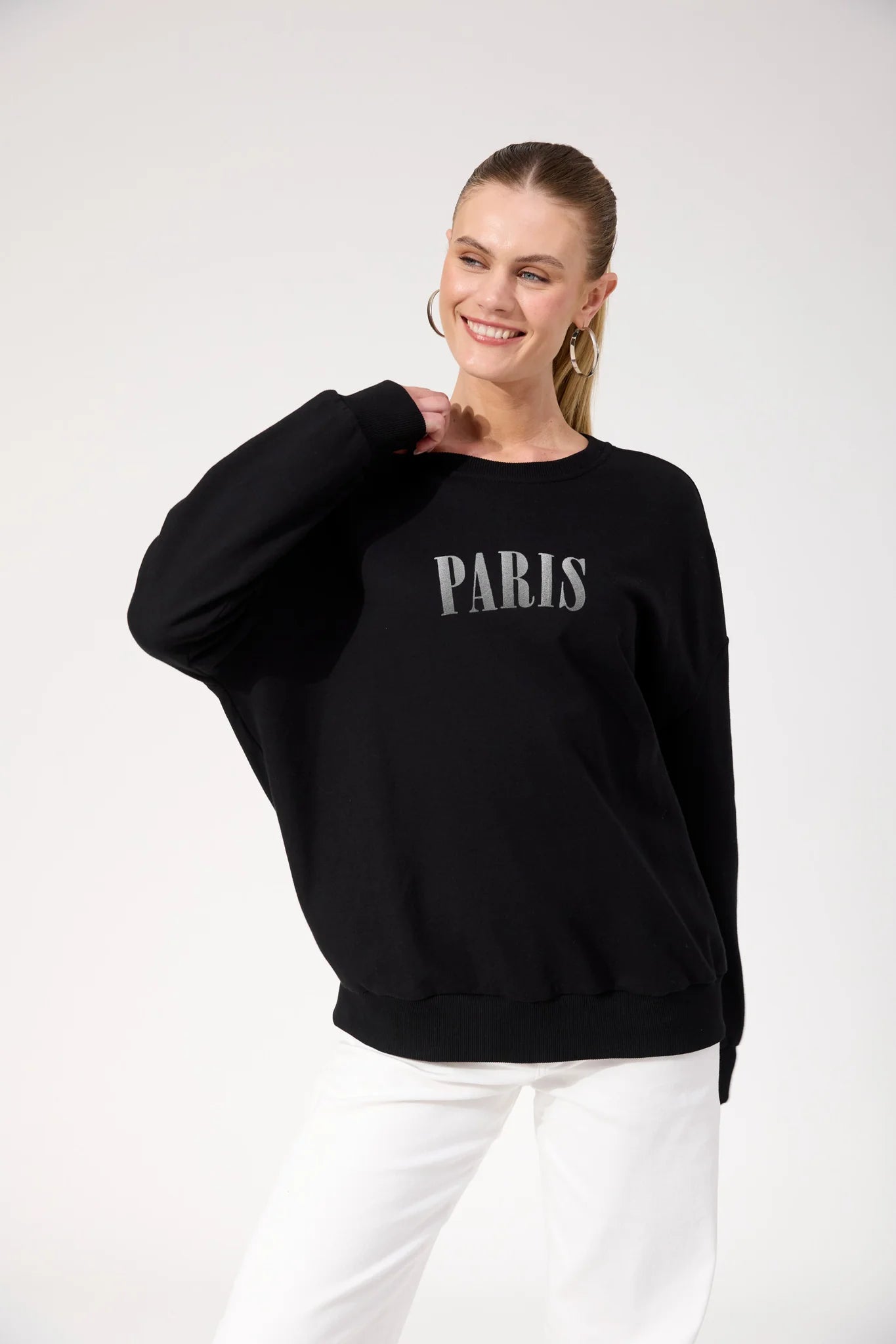 Image of Woman wearing Haven black crewneck paired with white pants on a plain background 