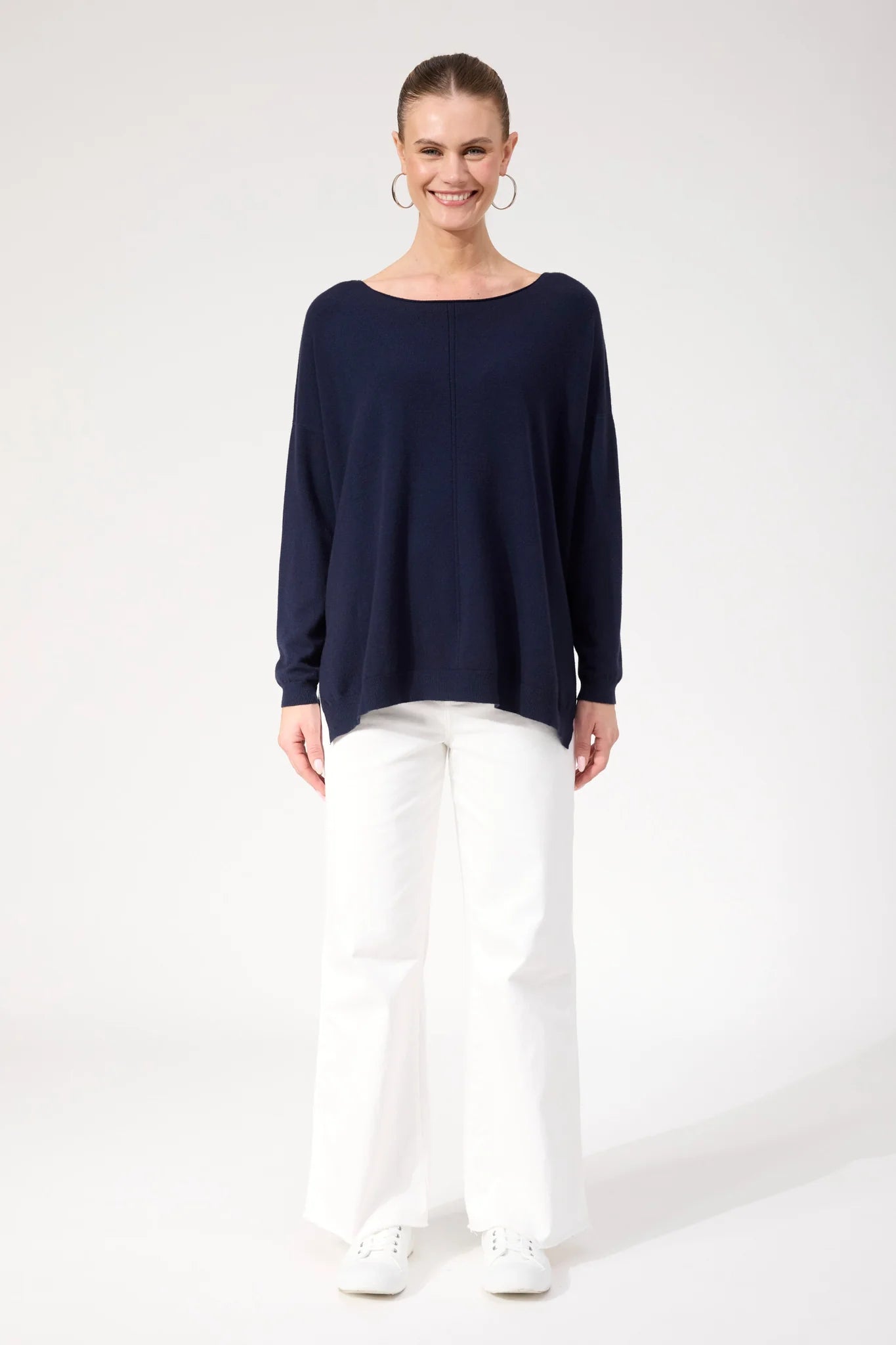 Image of Woman wearing Haven navy jumper paired with white jeans on a plain background