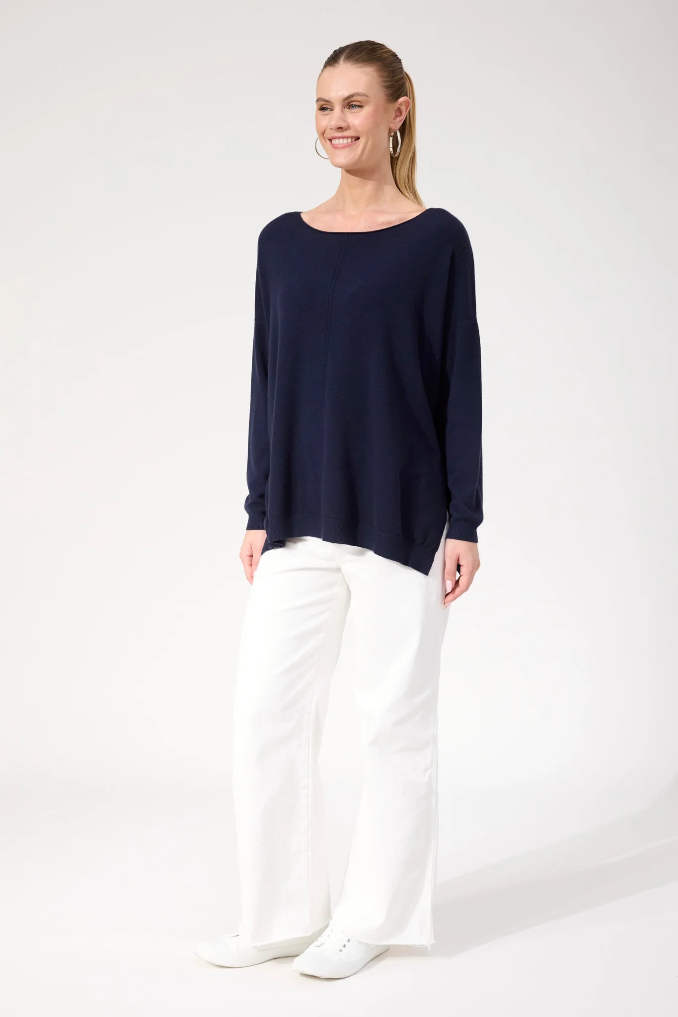 Image of Woman wearing Haven navy jumper paired with white jeans on a plain background