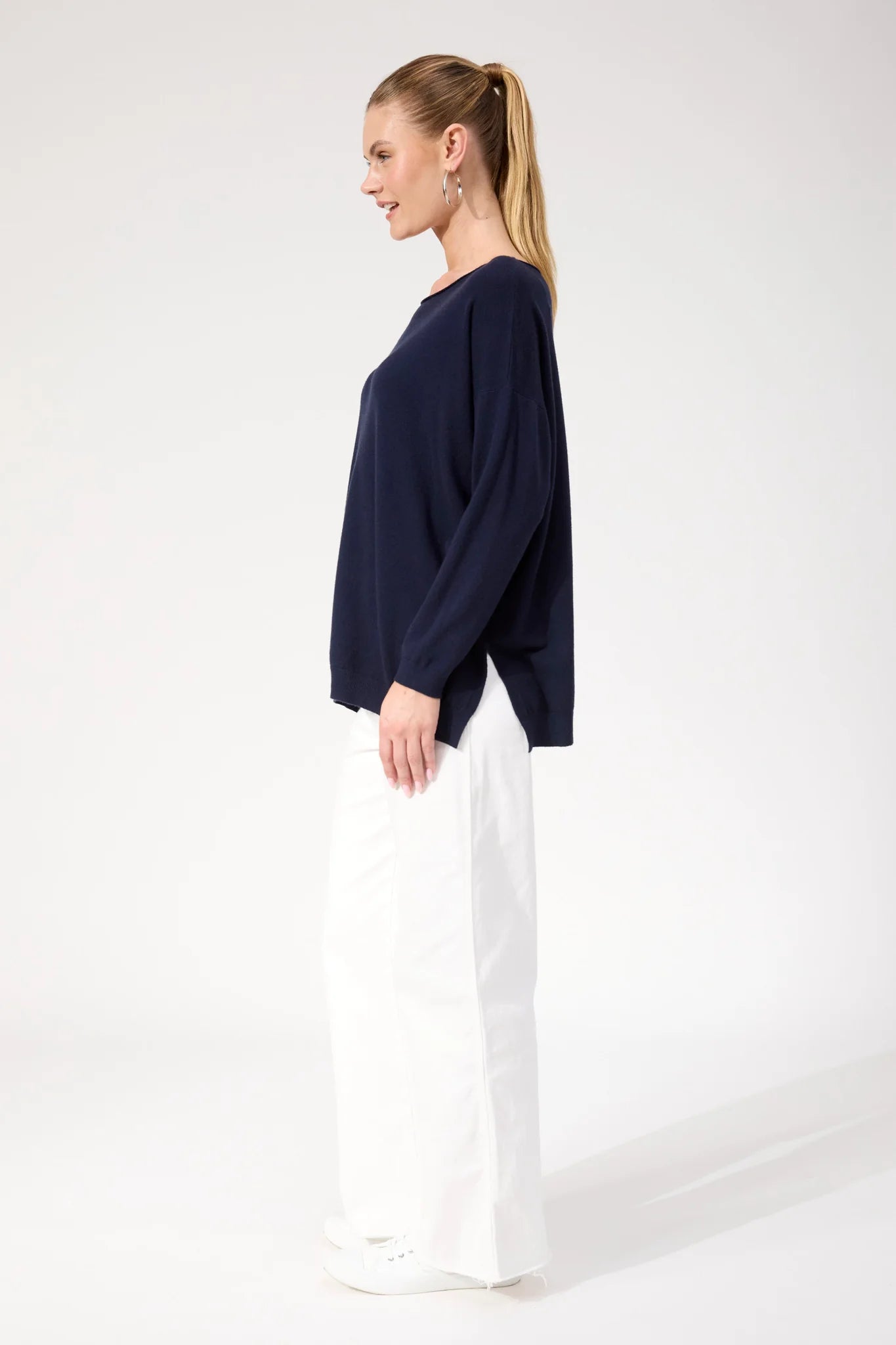 Woman wearing Haven navy jumper paired with white jeans on a plain background