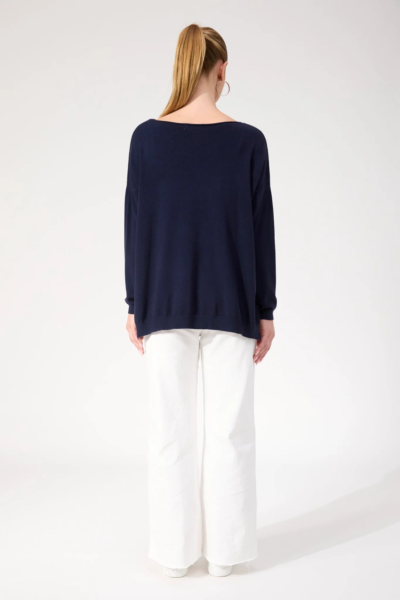 Image of Woman wearing Haven navy jumper paired with white jeans on a plain background