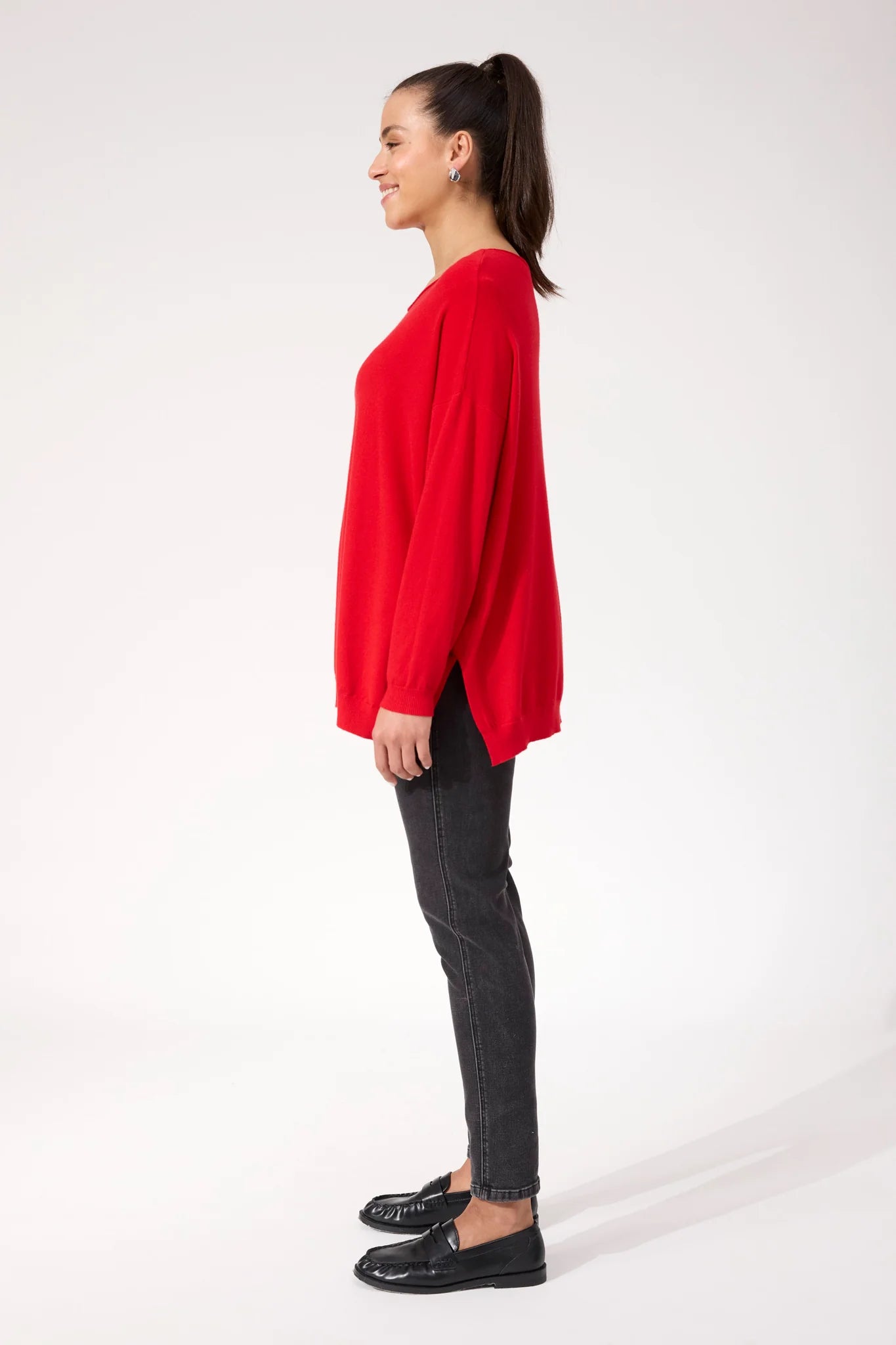 Image of Woman wearing red Haven knit paired with black denim jeans on a plain background