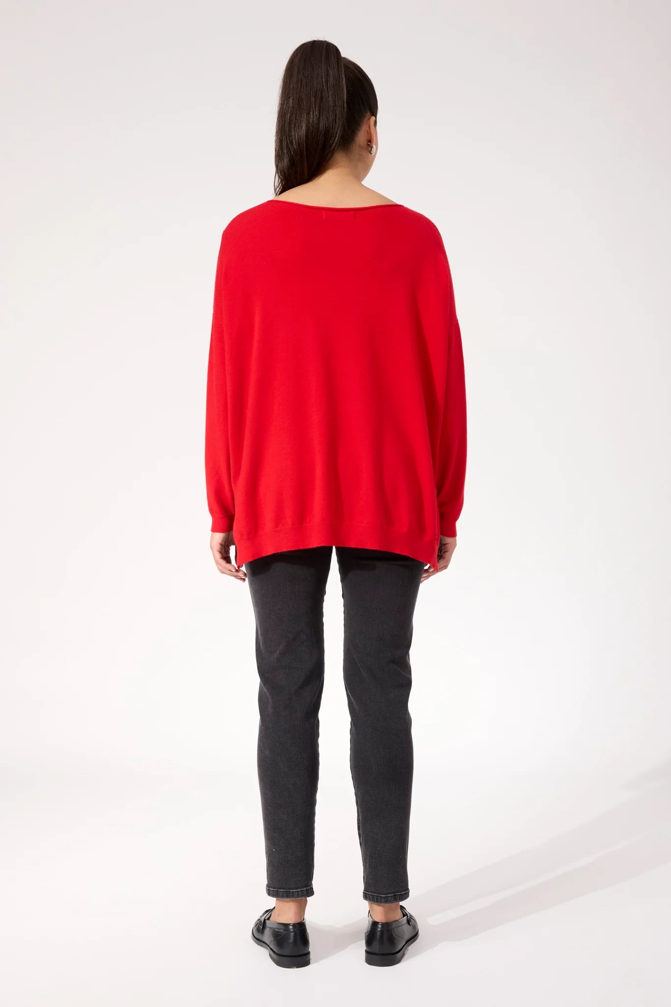 Image of Woman wearing red Haven knit paired with black denim jeans on a plain background